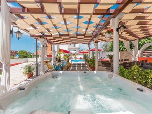 A hot tub area with a pool in the background, surrounded by outdoor seating and potted plants. - Villa Ancora for 16 guests,  No.1 by Interhome (Donje Rastane)