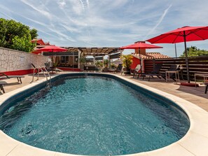 A swimming pool with a stone wall, lounge chairs, and red umbrellas. - Vacation home  by Interhome (Donje Rastane)