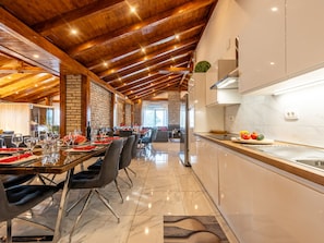 A spacious dining area with a high ceiling and exposed wooden beams, a modern kitchen with marble countertops, and a view of the outdoors. - Vacation home  by Interhome (Donje Rastane)