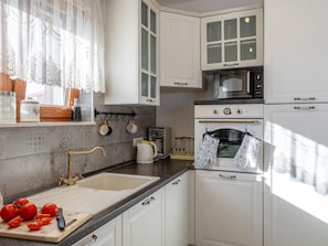 A kitchen with white cabinets, a sink, a stove, and a window with lace curtains. - Holiday Home Beti with heated pool by Interhome (Vrsi)