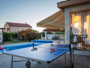Ett utomhusområde med en pool, ett bord för bordtennis, en överbyggd sittplats och ett hus i bakgrunden.