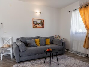 A living room with a grey sofa, a small table with a bowl of fruit, a painting on the wall, and a window with curtains. - Holiday Home Beti with heated pool by Interhome (Vrsi)
