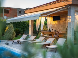 A poolside area with lounge chairs, a table, and a covered seating area with a TV. - Holiday Home Beti with heated pool by Interhome (Vrsi)