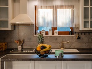 A kitchen with a fruit bowl on the counter, a green mug, and a window with curtains. - Holiday Home Beti with heated pool by Interhome (Vrsi)