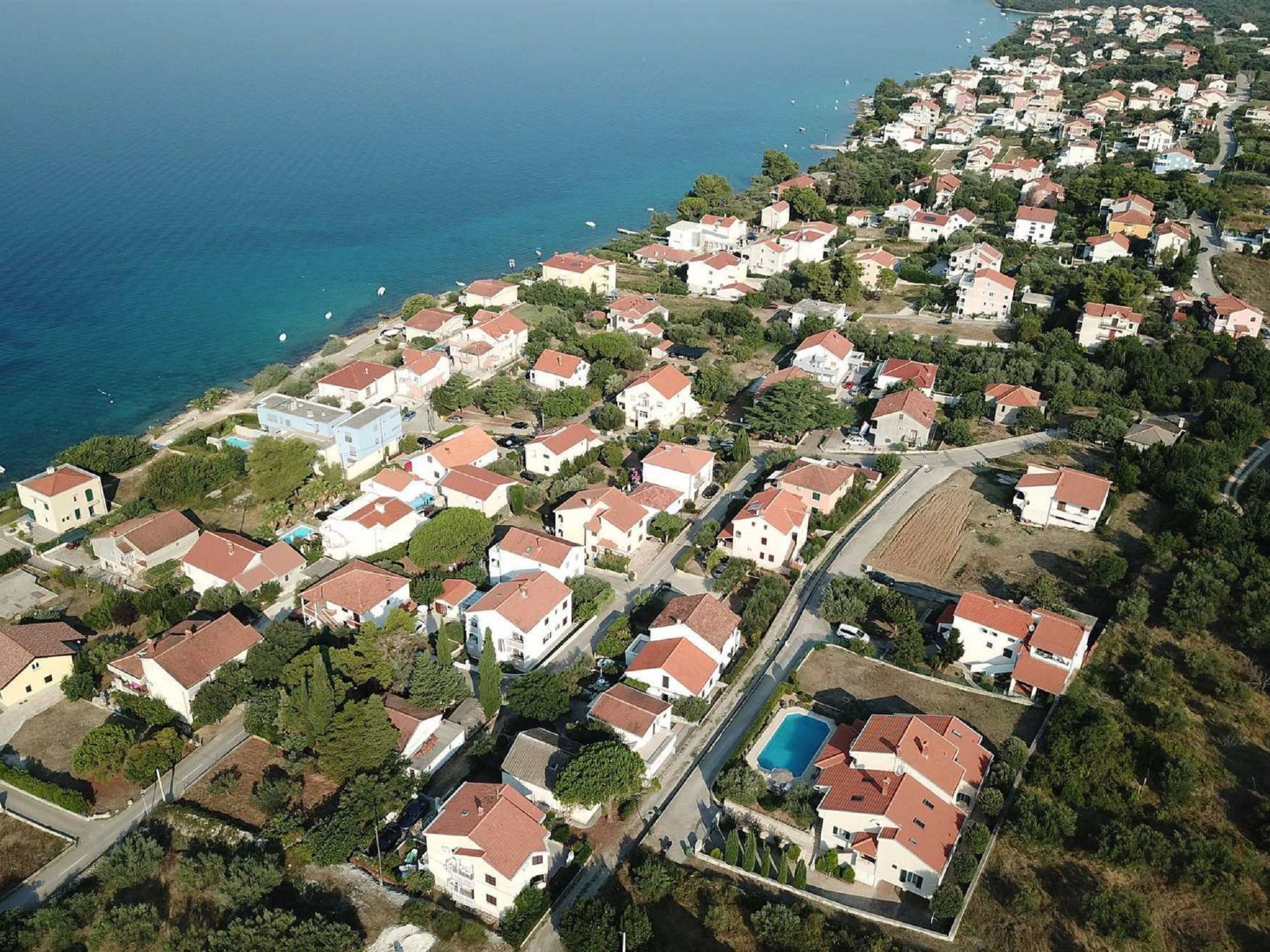 An aerial view of a coastal residential area with houses, roads, and a clear blue sea.