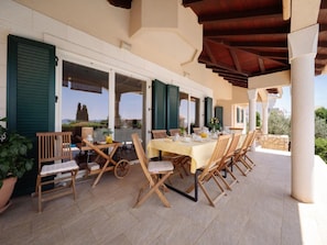 An outdoor dining area with a table set for six, surrounded by wooden chairs, under a covered patio with a view of the landscape. - Magnificent Villa Clara with big pool by Interhome (Petrčane)