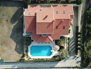 Um edifício de vários andares com piscina, cercado por vegetação e um acesso pavimentado.