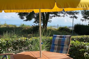 Un pontile in legno con un ombrellone giallo, una sedia a sdraio con cuscino a quadretti e vista sul mare e sulla terraferma in lontananza.
