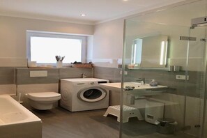 Un bagno moderno dotato di lavatrice, servizi igienici e cabina doccia in vetro.
