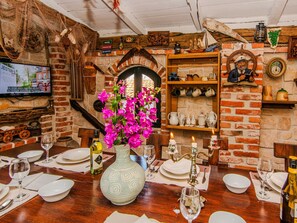 Comedor con pared de ladrillo, televisor y mesa dispuesta para una comida.