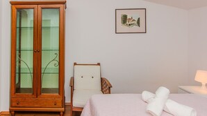 Makuuhuoneessa on puinen vaatekaappi, tuoli, sängyllä on rullalle taiteltuja pyyhkeitä, seinällä on kehystetty kuva ja yöpöydällä on lamppu.
