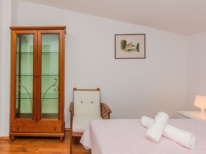 A bedroom with a wooden wardrobe, a chair, a bed with rolled towels, a framed picture on the wall, and a bedside lamp. - Vacation home  by Interhome (Rovanjska)