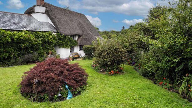 A thatched-roof house with a garden, a bench, and a pond. - Host & Stay | Wistermead Cottage (Dolton)
