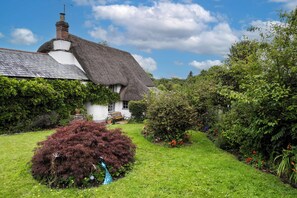A thatched-roof house with a garden, a bench, and a pond. - Host & Stay | Wistermead Cottage (Dolton)