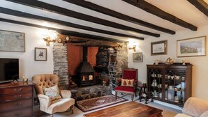 A traditional room with exposed beams, a stone fireplace, a television, a wooden coffee table, and a red armchair. - Host & Stay | Wistermead Cottage (Dolton)