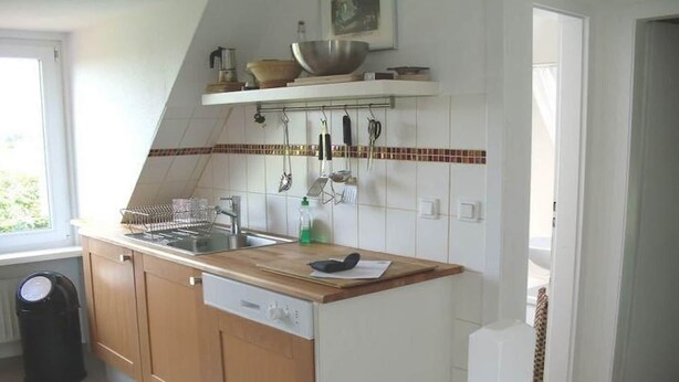 A kitchen with wooden cabinets, a dishwasher, a sink, and a window. - Ferienhaus in Püttsee auf Fehmarn (Püttsee)