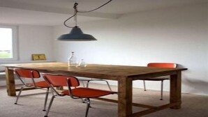 A dining area with a wooden table, two red chairs, a hanging light fixture, and a window in the background. - Ferienhaus in Püttsee auf Fehmarn (Püttsee)
