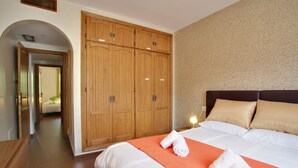 A hotel room with a large wooden wardrobe, a bed with white linens, and a bright wall. - Two-Bedroom Benahavis Village Apartment with beautiful Mountain View. (Benahavís)