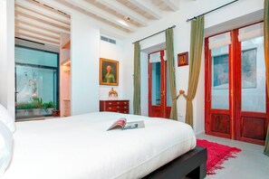 A bedroom with a bed, a wooden dresser, a framed picture on the wall, and a red door.