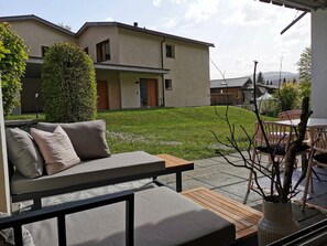 A modern outdoor seating area with a sofa and table, a well-maintained lawn, and a building in the background. - Abitaziun Patgific - Ferienwohnung im Casa Hirundella, (Trin Mulin), by Interhome (Trin)