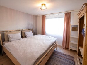 Un dormitorio con cama, armario y ventana con cortinas.
