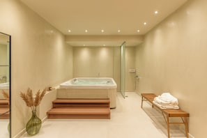 A modern bathroom with a bathtub, a glass shower enclosure, a wooden bench, and a vase with dried plants.