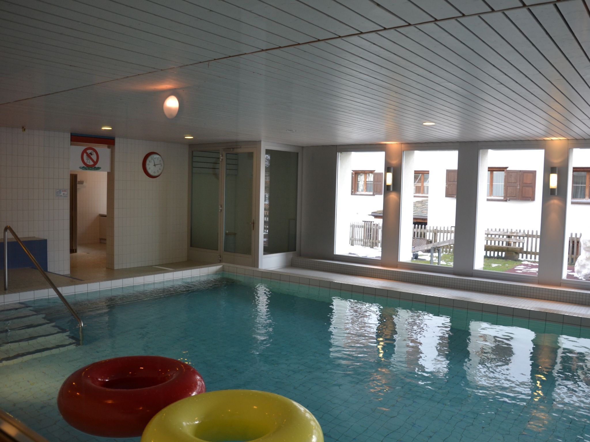 Une piscine intérieure avec des parois en verre transparent, une horloge bien visible et un panneau indiquant qu'il est interdit de fumer.