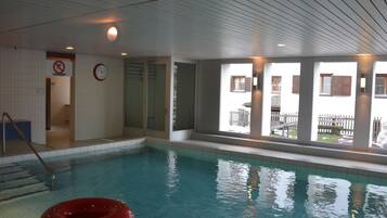 Une piscine intérieure avec des parois en verre transparent, une horloge bien visible et un panneau indiquant qu'il est interdit de fumer.