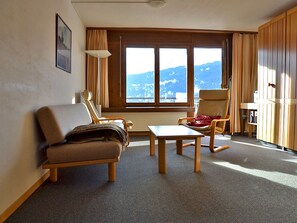 A room with a sofa, two armchairs, a small table, a window with a mountain view, and wooden paneling.