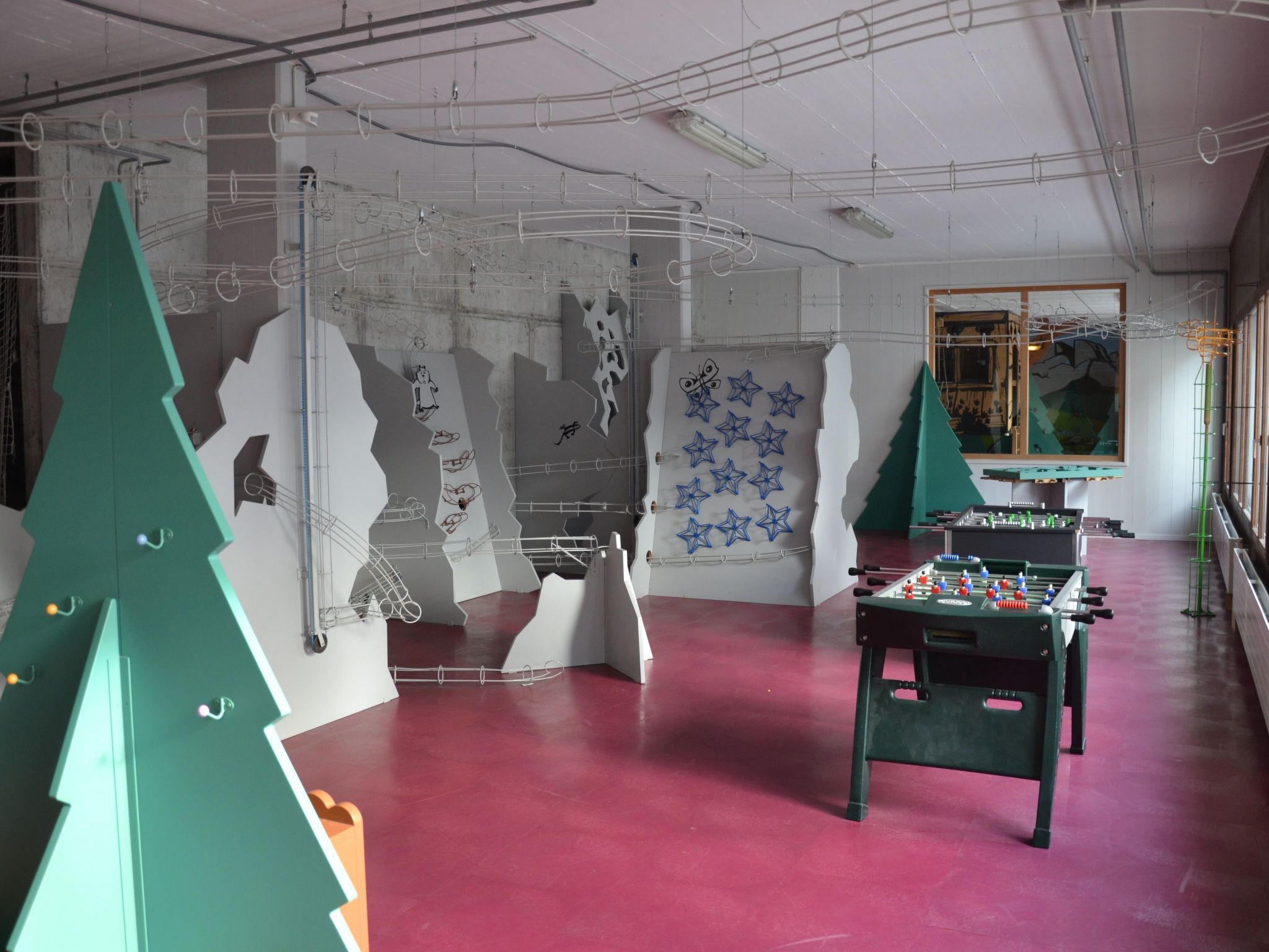 Un espace intérieur agrémenté d’un baby-foot, de décorations de Noël vertes et d’œuvres d’art abstraites sur les murs.