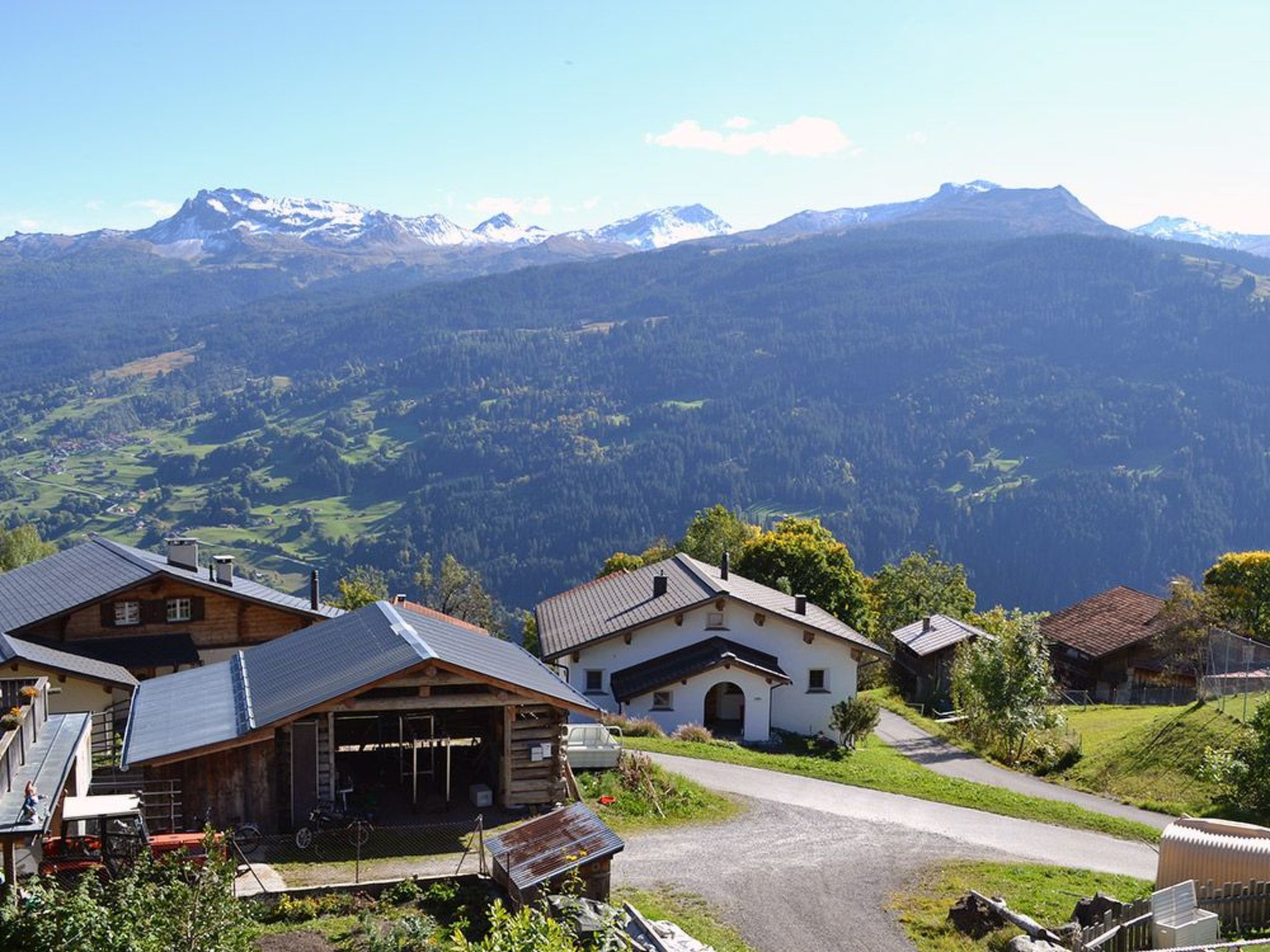 A mountain village with traditional wooden houses, a paved road, and a view of snow-capped mountains.