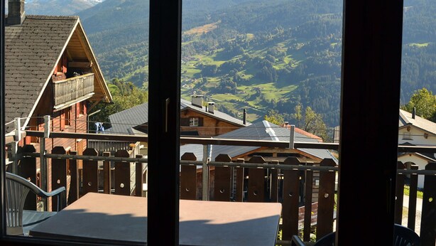 Bergzicht vanaf een balkon met een houten hut en een stoel.