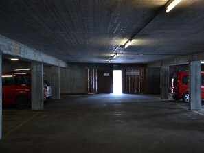 Eine Tiefgarage mit Betonpfeilern, einem roten Auto und einem Schild, das eine Rampschranke anzeigt.