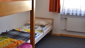 Een kamer met stapelbedden, een radiator, een raam met gordijnen en een hanglamp.