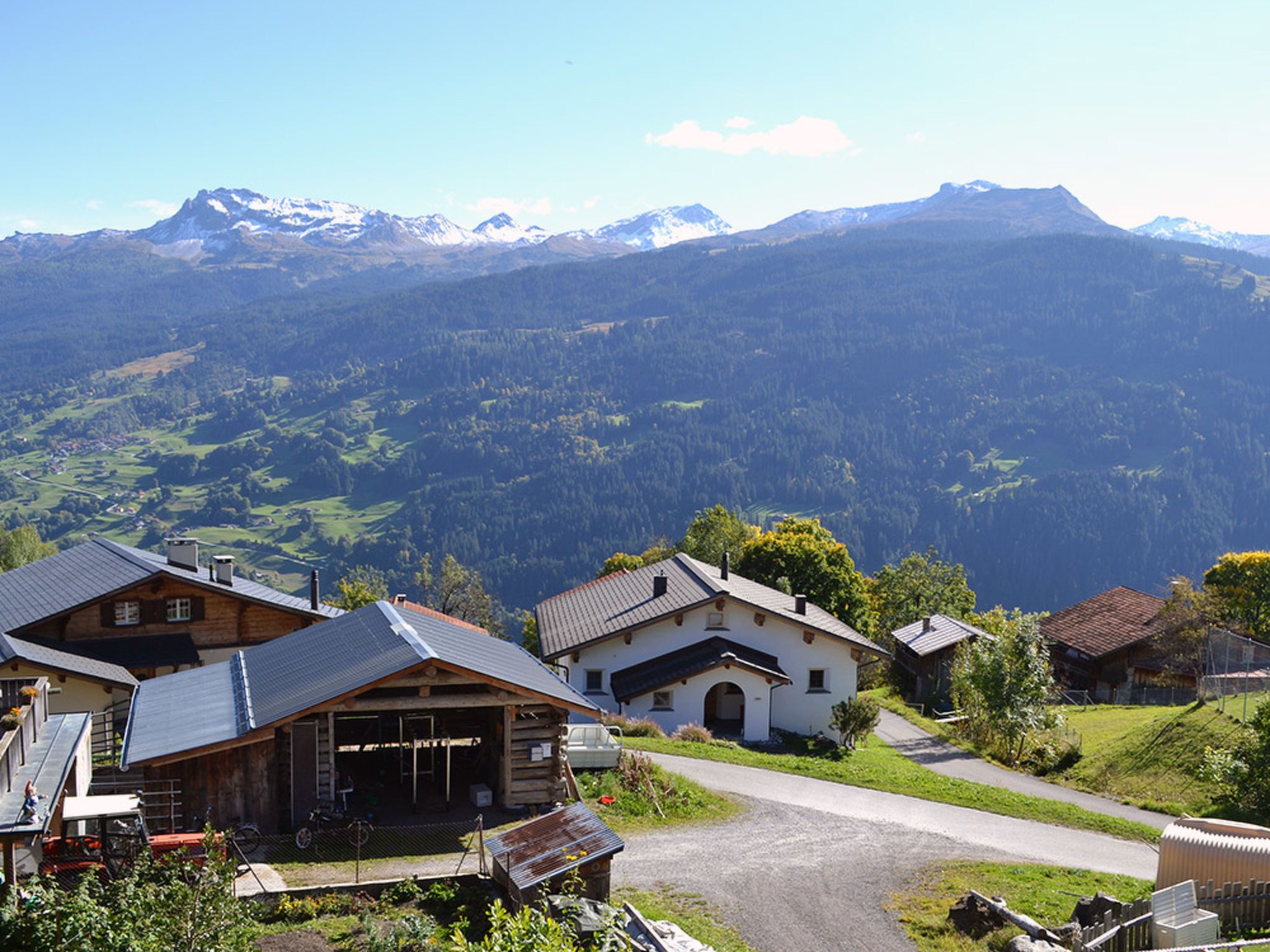 Een bergdorpszicht met traditionele houten huizen, een geplaveid weggetje en besneeuwde bergtoppen.