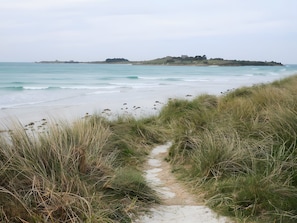 A coastal path leading to a beach with a distant hill and a building.