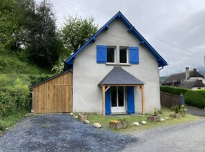 Ein zweistöckiges Haus mit Holztür zur Garage, einer kleinen Veranda mit blauen Fensterläden und einem Schotterweg.
