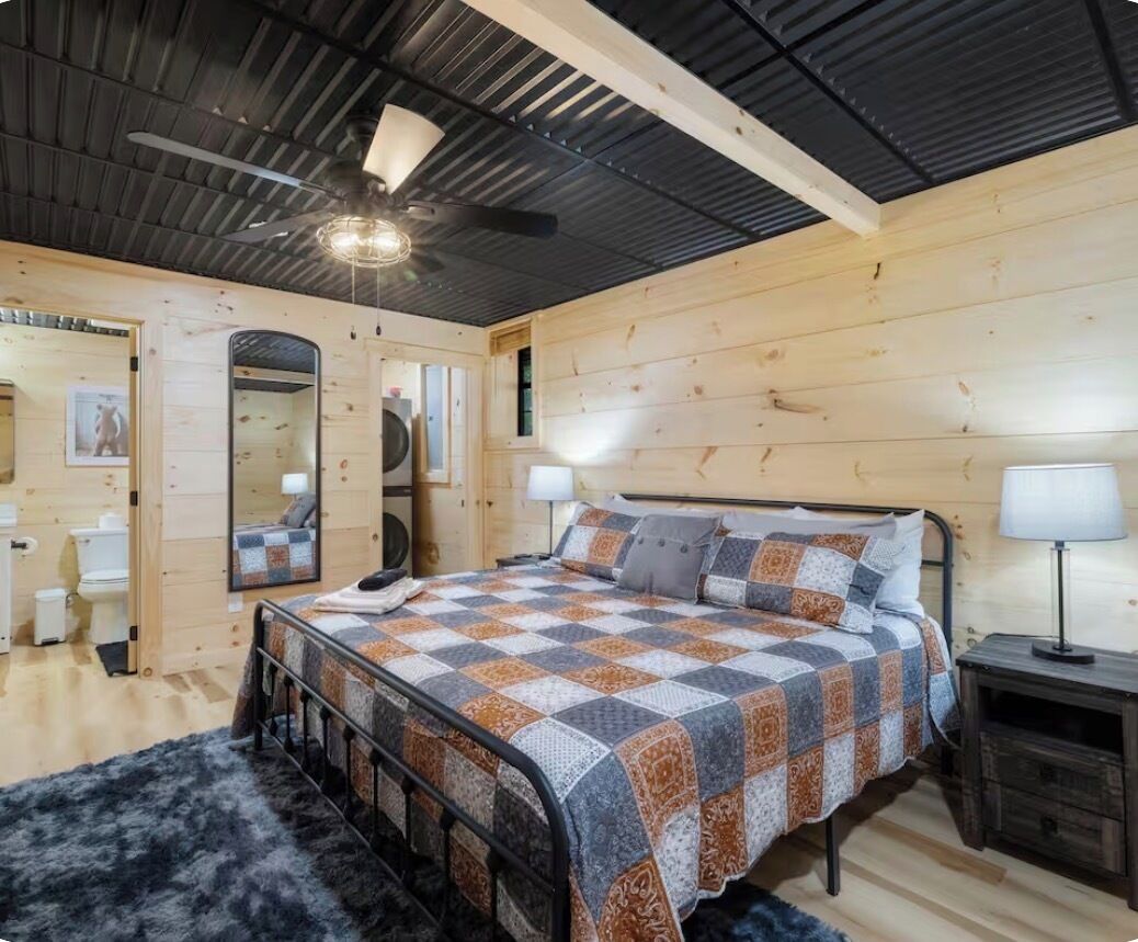 Une chambre à coucher avec un lit, un ventilateur de plafond, un miroir et un mur en bois.