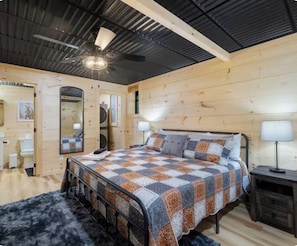 Ein Schlafzimmer mit einem Bett, einem Deckenventilator, einem Spiegel und einer Holzwand.
