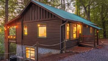 A rustic cabin with a metal roof, a front porch, and a small deck.