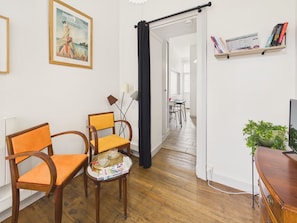 A room with wooden flooring, a dining table with chairs, a bookshelf, a television, and a framed picture on the wall. - 400 m from the beach, apartment for 2 (Dinard)