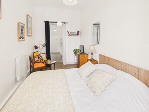 Hotellihuone, jossa on suuri sänky, työpöytä tietokoneella, tuoli, patteri ja kirjahylly.