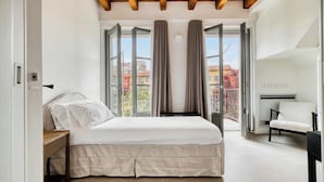 A bedroom with a bed, a nightstand, a chair, and a view of buildings through large windows. - w* | Luxury 5BR Retreat near Navigli (Milano)