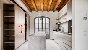A modern kitchen with a marble island, wooden ceiling beams, and built-in cabinets. - w* | Luxury 5BR Retreat near Navigli (Milano)