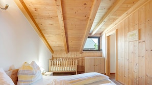 Una habitación con paneles de madera, una cuna, una cama con almohadas y una ventana.