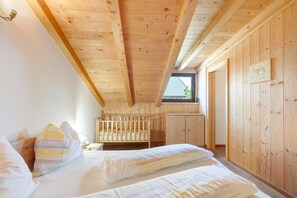 Ein Zimmer mit Holzwänden, einem Kinderbett, einem Bett mit Kissen und einem Fenster.