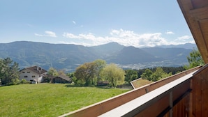 Vista desde un balcón con paisaje montañoso, una casa y árboles.