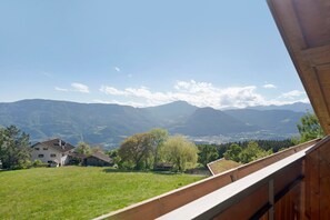 Blick vom Balkon auf eine gebirgige Landschaft mit Haus und Bäumen.