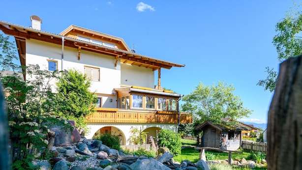 Una casa de dos pisos con balcón, rodeada por un jardín con rocas y plantas.