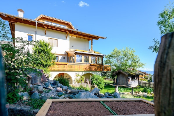 Ein zweistöckiges Haus mit einem Balkon, umgeben von einem Garten mit Steinen und Pflanzen.